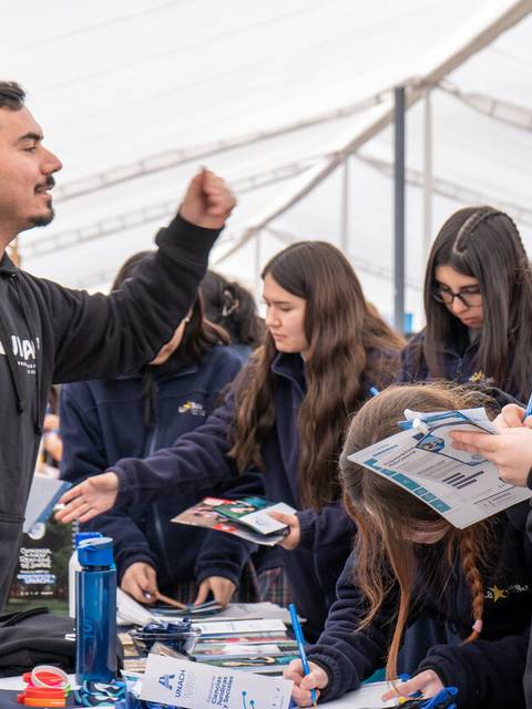 Un grupo de personas jóvenes interactuando en un evento, donde un hombre parece estar dando una charla apasionada mientras otros toman notas.