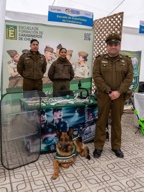 Un grupo de carabineros chilenos posando en un stand de la Escuela de Suboficiales de Carabineros de Chile con un perro de trabajo.