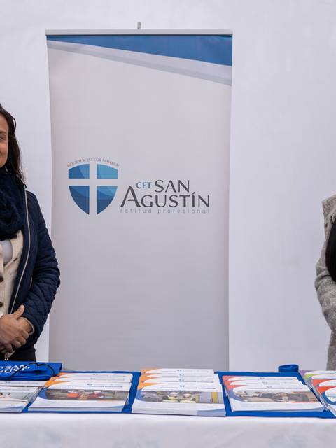 Dos mujeres sonrientes están de pie detrás de un mostrador con productos y un banner del CET San Agustín.