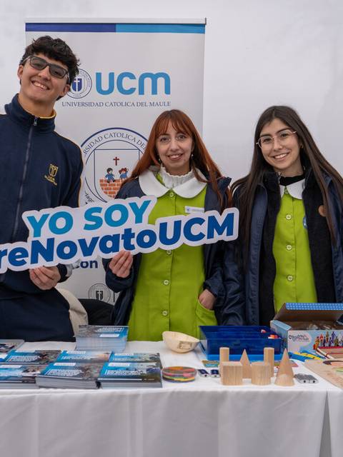 Estudiantes posan en un stand de promoción de la UCM con materiales educativos y una pancarta.