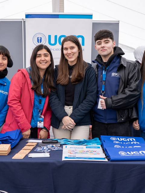 Un grupo de jóvenes posan frente a una mesa con materiales promocionales de la UCN en un evento.