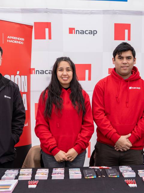Un grupo de cuatro personas sonrientes posan frente a un mostrador con material promocional de la institución Inacap.