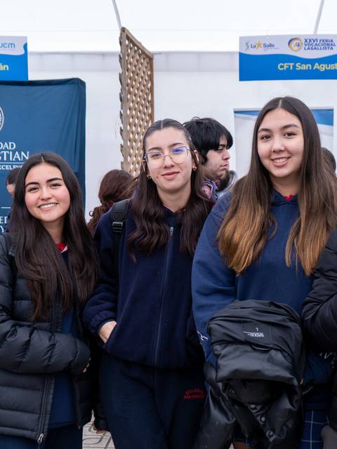 Un grupo de cinco jóvenes sonríen frente a un stand en un evento educativo.
