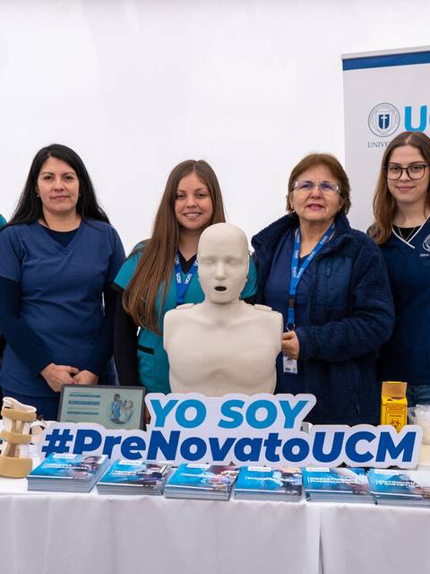 Un grupo de cinco personas sonríen junto a una mesa con material de promoción de una universidad.
