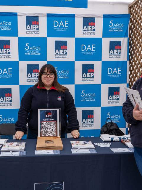 Dos personas están de pie en un stand con materiales promocionales de AIEP.