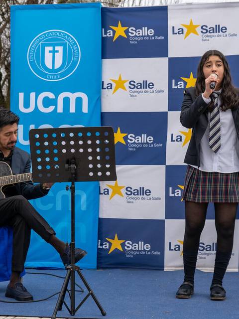 Una niña canta mientras un guitarrista la acompaña en un evento al aire libre.