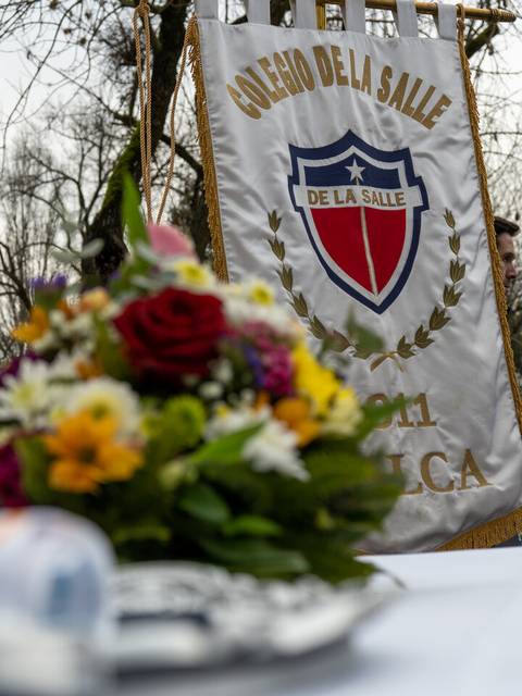 Una bandera con el escudo de un colegio y un ramo de flores en primer plano.