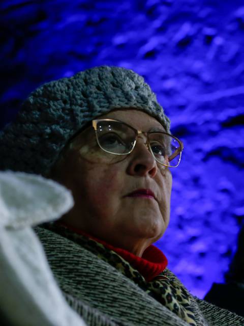 Una mujer mayor con gorro y gafas observa atentamente en un ambiente iluminado de manera tenue.