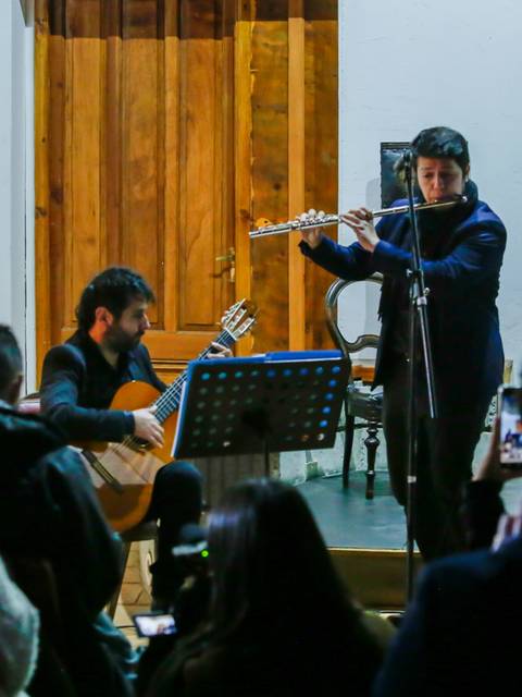 Un recital de música en vivo donde un flautista y un guitarrista actúan frente a una audiencia.