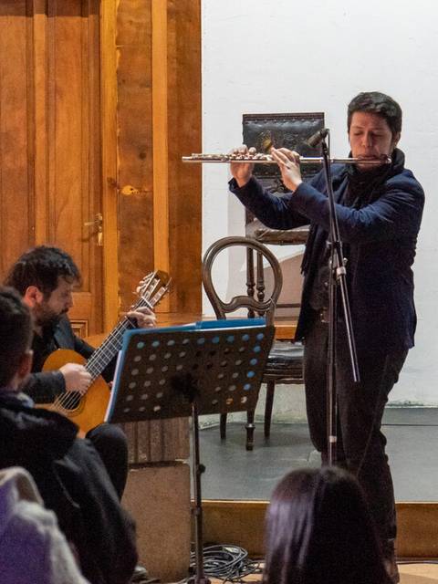 Un músico toca la flauta en un escenario frente a un público atento.