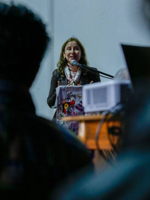 Una mujer está hablando frente a un micrófono en un evento o conferencia.