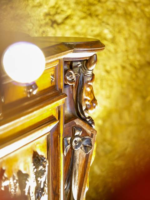 Una imagen que muestra un detalle de un mueble tallado con una iluminación suave de fondo.