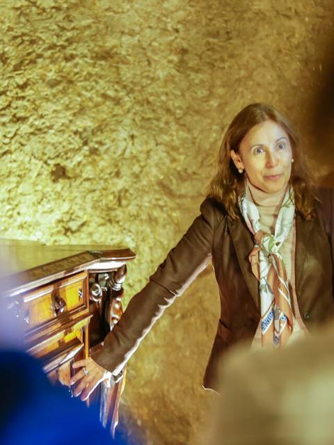 Una mujer está de pie junto a un sarcófago en un ambiente iluminado con luces cálidas.