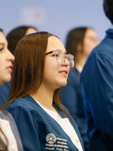 Un grupo de estudiantes con chaquetas azules se encuentra escuchando atentamente en un evento.
