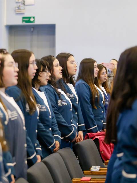 Un grupo de mujeres de pie, vestidas con chaquetas azules, asistiendo a un evento.