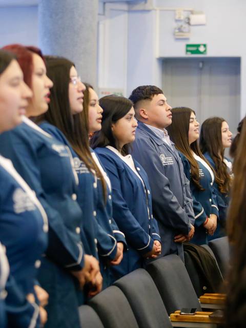 Un grupo de jóvenes de pie, vistiendo chaquetas azules, se encuentran en una ceremonia formal.