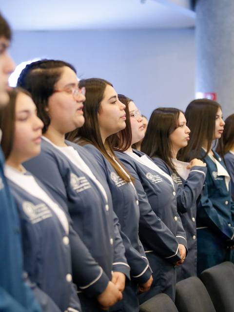 Un grupo de estudiantes de pie, vestidos con chaquetas azules, en un evento formal.