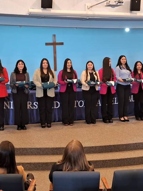 Ceremonia de entrega de diplomas a un grupo de graduadas en un auditorio institucional.