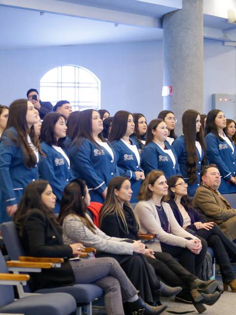 Un grupo de personas en un evento en un auditorio, con mujeres en pie al frente y un público sentado detrás.