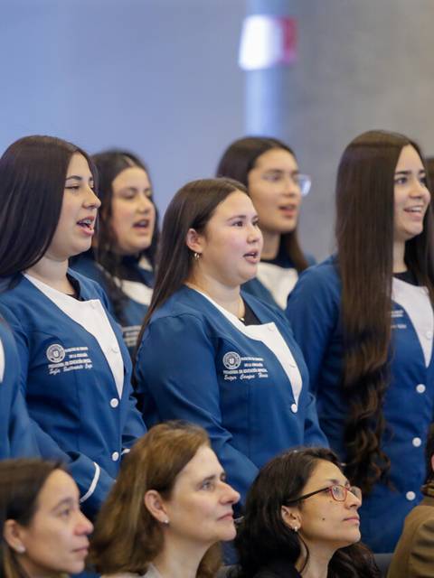 Un grupo de mujeres en uniformes azules canta frente a un público en un evento.