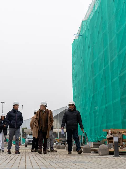 Un grupo de personas camina por un sitio de construcción con un edificio cubierto por una malla verde.