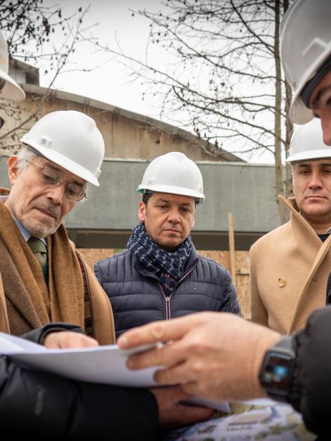 Un grupo de personas con cascos de seguridad revisando planos en una obra de construcción.