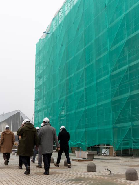 Un grupo de personas camina hacia un edificio en construcción cubierto con una red verde.