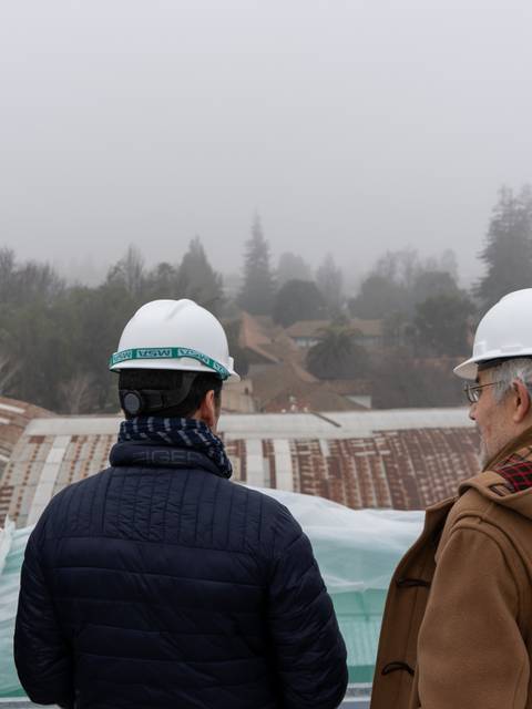 Tres personas con cascos de seguridad observan un paisaje urbano en un día neblinoso.