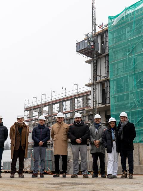 Un grupo de personas con cascos se encuentra frente a un edificio en construcción cubierto con una malla verde.