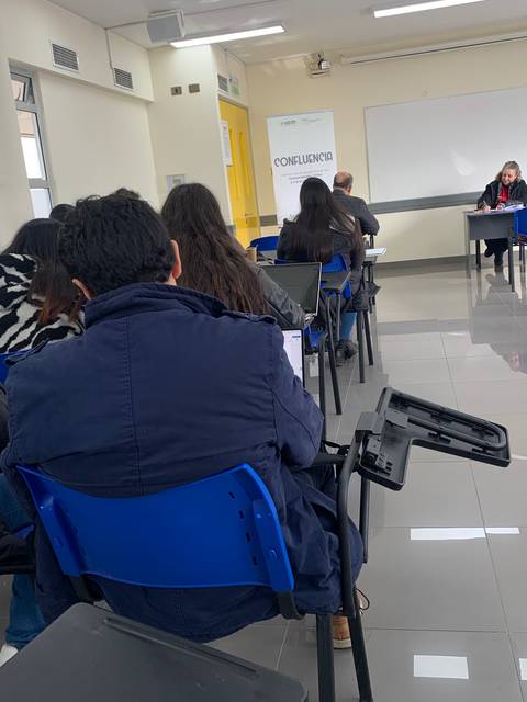 Un grupo de personas asiste a una reunión en una sala con escritorios y sillas azules.