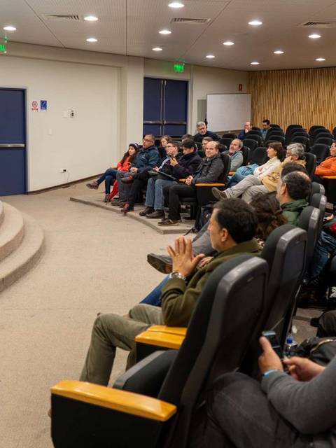 Un auditorio lleno de personas escuchando a una ponente en un escenario.