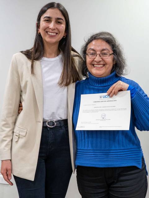 Dos mujeres posan sonrientes, una de ellas sostiene un certificado.