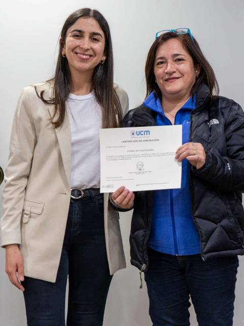 Dos mujeres sonríen mientras sostienen un certificado en un ambiente interior.