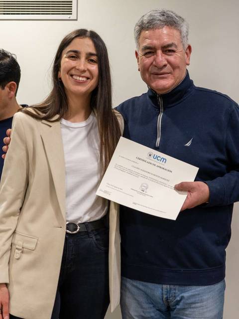 Una joven y un hombre mayor posan juntos sosteniendo un certificado de entrega en un evento.