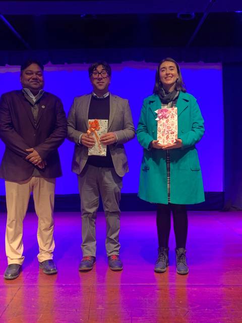 Tres personas posan sonrientes en un escenario iluminado con luz azul.