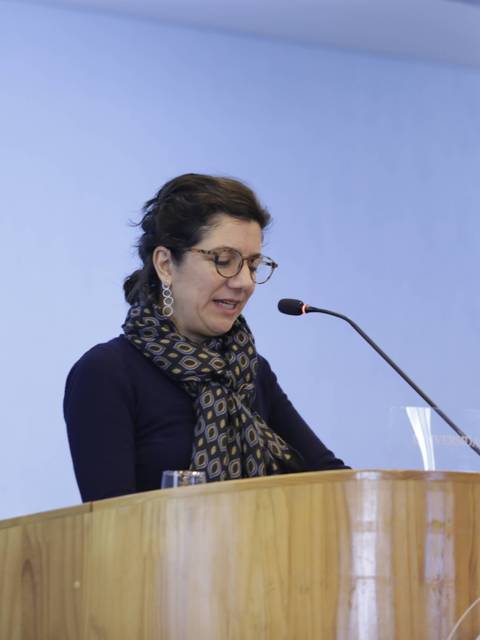 Una mujer se encuentra hablando en un podio frente a una bandera chilena.