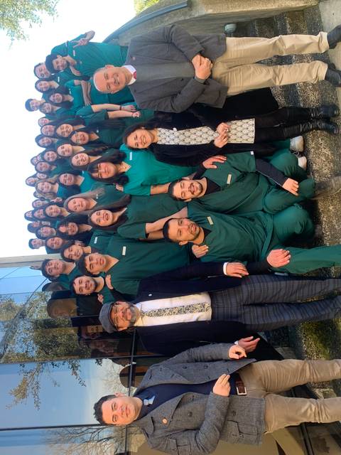 Un grupo de personas en uniformes verdes posan juntas frente a un edificio con grandes ventanas.
