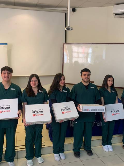 Un grupo de estudiantes de medicina veterinaria posan con cajas en un evento educativo.