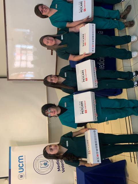 Un grupo de cinco personas vestidas con uniformes de color verde sosteniendo cajas en un evento.