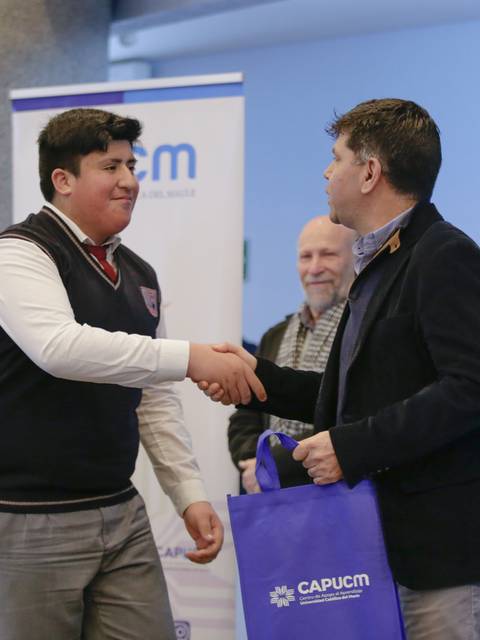 Un joven estrecha la mano de un adulto en un evento, mientras otros observan.