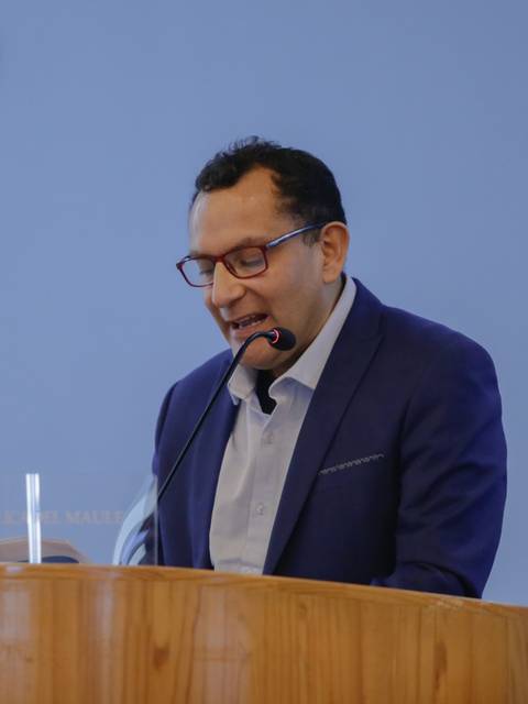 Un hombre está dando un discurso en un escenario con una cruz en el fondo y una bandera chilena al costado.