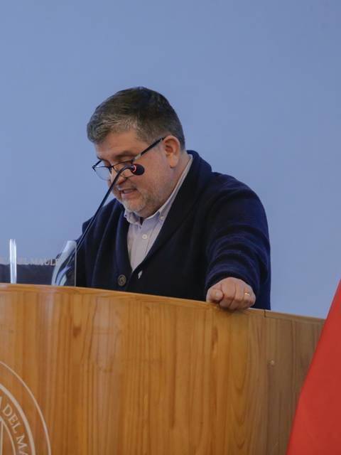 Un hombre está hablando desde un podio en un evento con una bandera chilena de fondo.