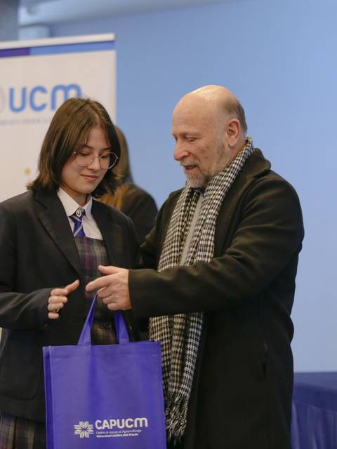 Un joven recibe una bolsa de regalo de manos de un adulto en un evento formal.