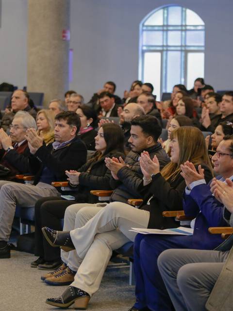 Un público aplaudiendo durante un evento en una sala llena de asistentes.