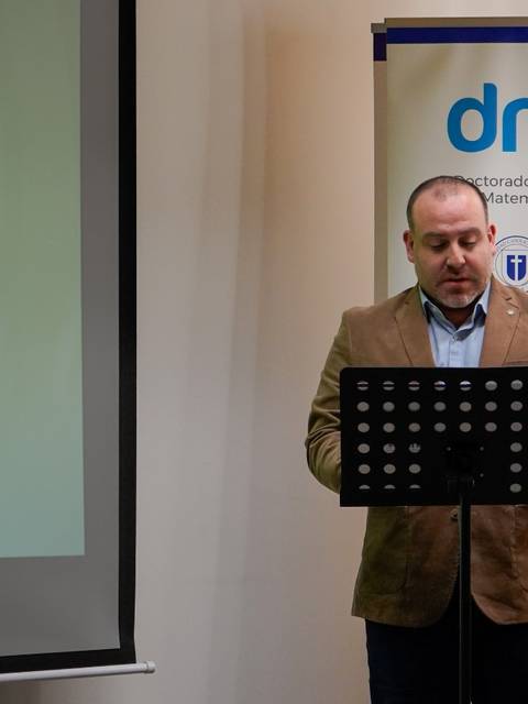 Una persona presenta un tema en un evento académico con un proyector y una pantalla detrás.