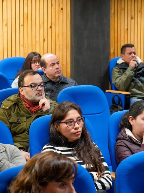 Un grupo de personas sentadas en un auditorio, escuchando atentamente una presentación.