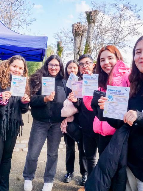 Un grupo de seis jóvenes sonrientes sosteniendo folletos en un evento al aire libre.