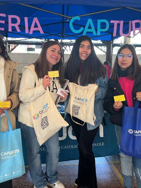 Cuatro jóvenes sonrientes posan frente a un stand universitario durante una feria de captación.
