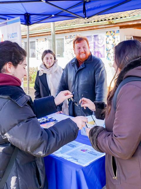 Un grupo de estudiantes interactúa en un stand en un evento al aire libre.