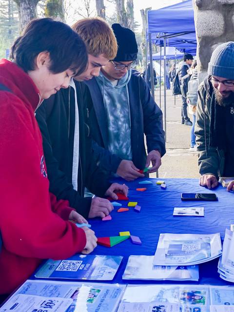 Un grupo de cuatro personas interactuando y jugando con bloques de colores sobre una mesa al aire libre.